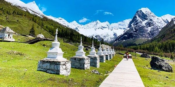 Alpine meadow trail and white stupas in Siguniang Mountain National Forest Park with four snow peaks