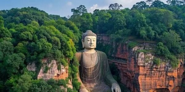 Leshan Giant Buddha full stone statue carved into red cliffs surrounded by forest, UNESCO World Heritage site in Sichuan