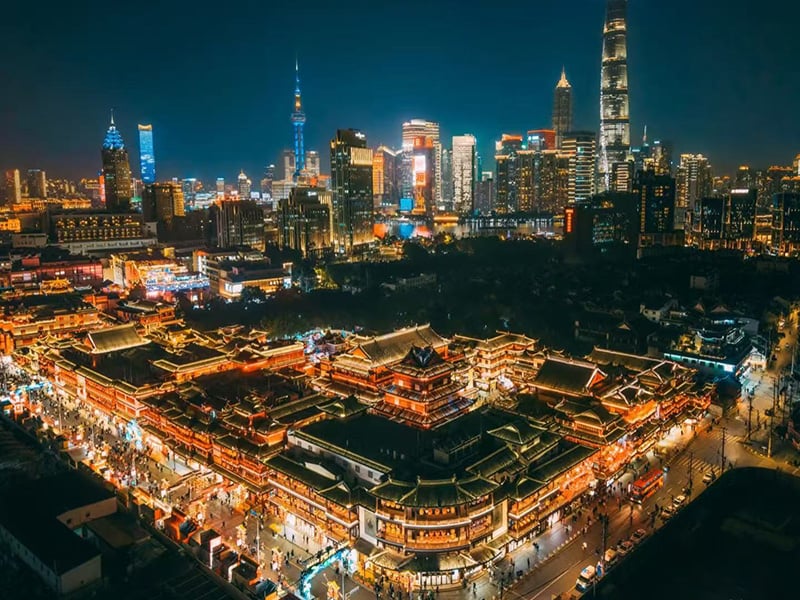 Night view of Yuyuan Bazaar traditional architecture glowing with lights against modern skyline.